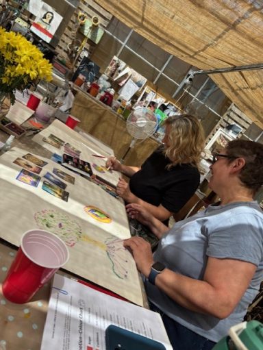 Two women engaged in art activities at a crafting table, surrounded by supplies.