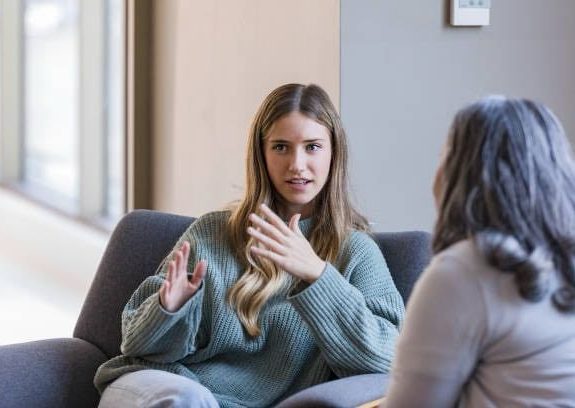 Two women engaged in conversation, one gesturing with her hands.