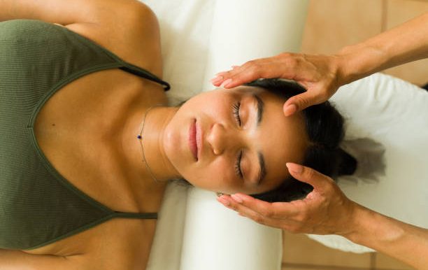 A person receiving a Reiki with their eyes closed and hands close to their face and their head.