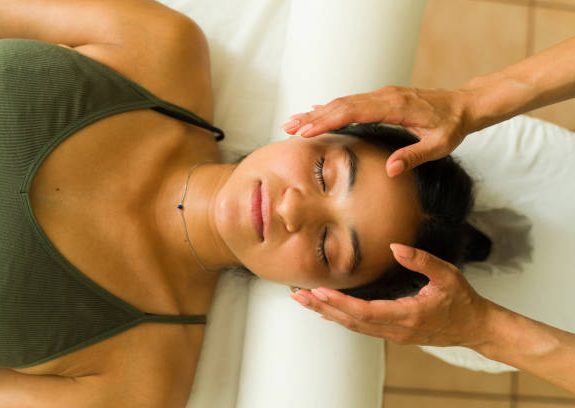 A person receiving a Reiki with their eyes closed and hands close to their face and their head.