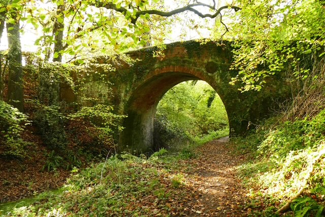 Stone bridge arching over a path surrounded by lush green foliage.