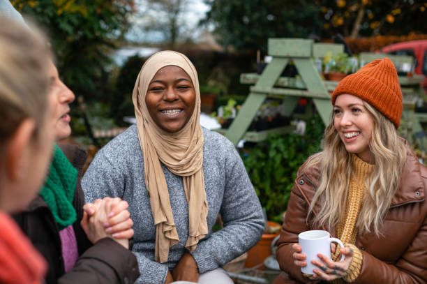 Group of four women chatting, enjoying a garden setting in autumn attire.