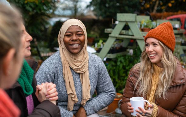 A group of four women chatting and smiling in a garden setting.