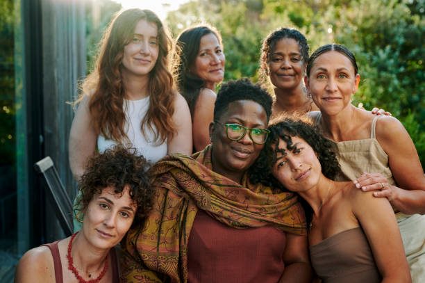 A group of diverse women smiling together in a sunny outdoor setting.