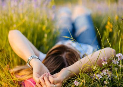A person lying in a meadow, relaxed with hands behind their head, surrounded by flowers.