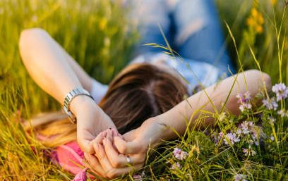 A person relaxing on a grassy field with arms behind their head surrounded by flowers.