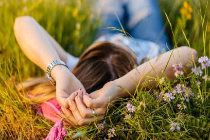 Person lying in a field of grass and wildflowers, hands clasped behind their head.