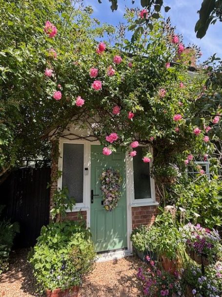 Quaint green door framed by lush foliage and pink flowers.