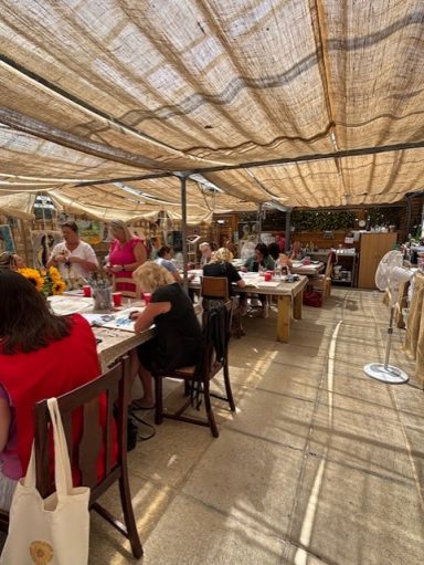 A busy outdoor dining area with people seated at tables under a sunshade.