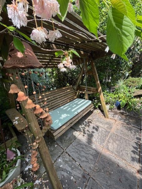 A wooden swing under greenery with blooming flowers nearby.