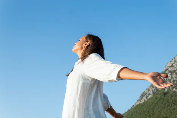 Somatic Resillience A woman with arms outstretched, enjoying the outdoors against a clear blue sky.
