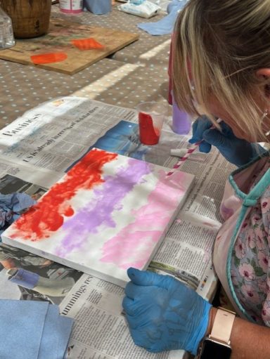 Person wearing gloves paints a canvas with red, pink, and purple colours.