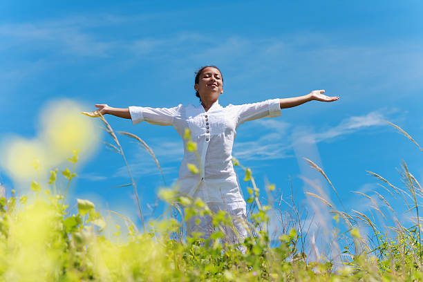 A woman with arms outstretched, enjoying the outdoors against a clear blue sky.