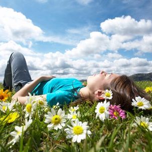 Hypnosis downloads A person lying on grass surrounded by colourful flowers under a cloudy sky.
