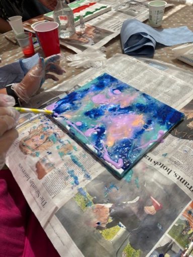 A person painting on a canvas with vibrant colours, surrounded by art supplies and newspaper.