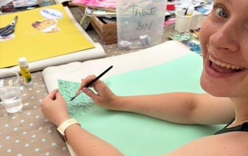 Phiona Hutton Counsellor and Integrative therapist, in person Havant, Hampshire or online nationwide. A person smiling while sketching on green paper with various art supplies around.