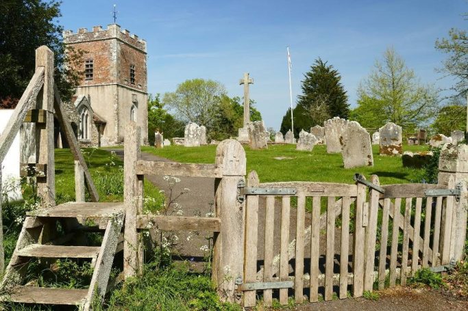 A rural graveyard with old gravestones and a stone church in the background.