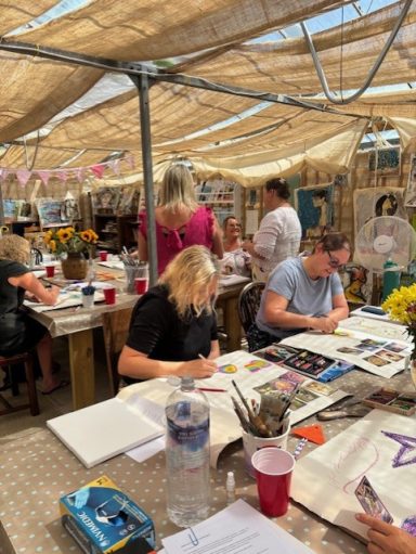 Artists working on their projects in a sunlit studio with tables and art supplies.