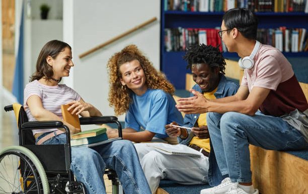 Four diverse young adults engage in conversation, one in a wheelchair, in a cozy setting.